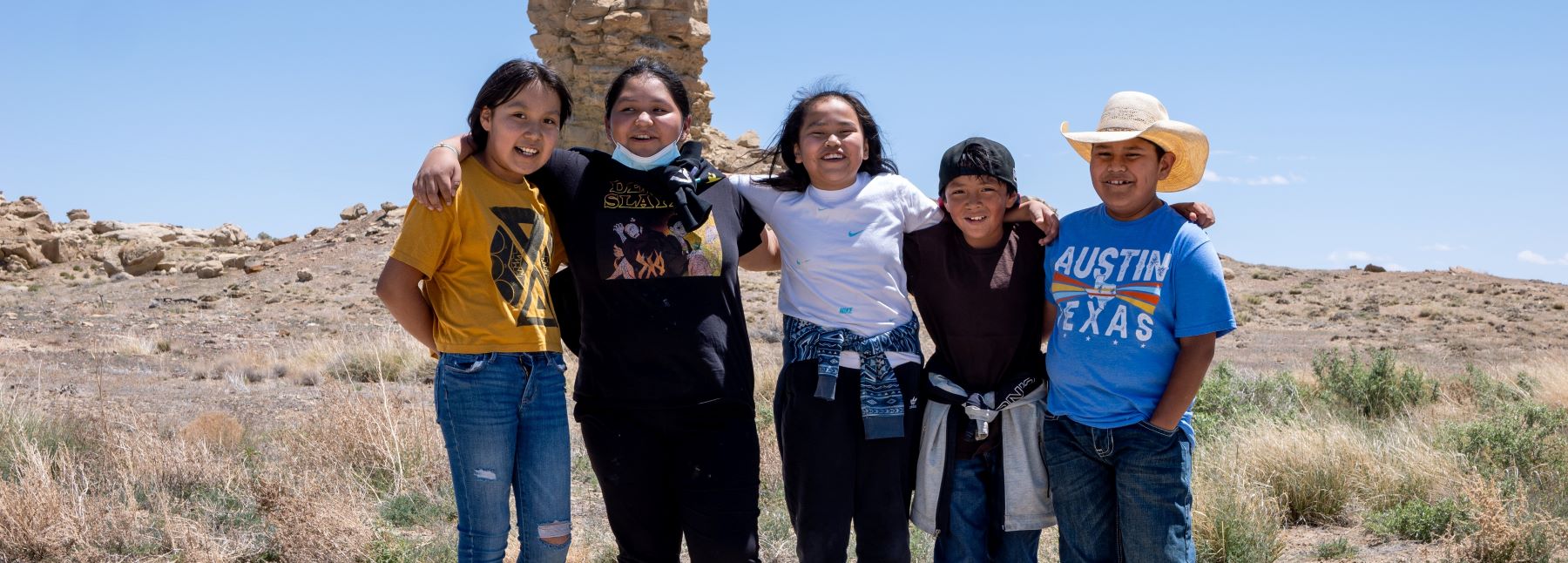 Five smiling students standing together outside.