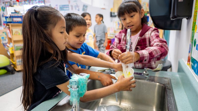 Students washing their paint supplies in the sink together.