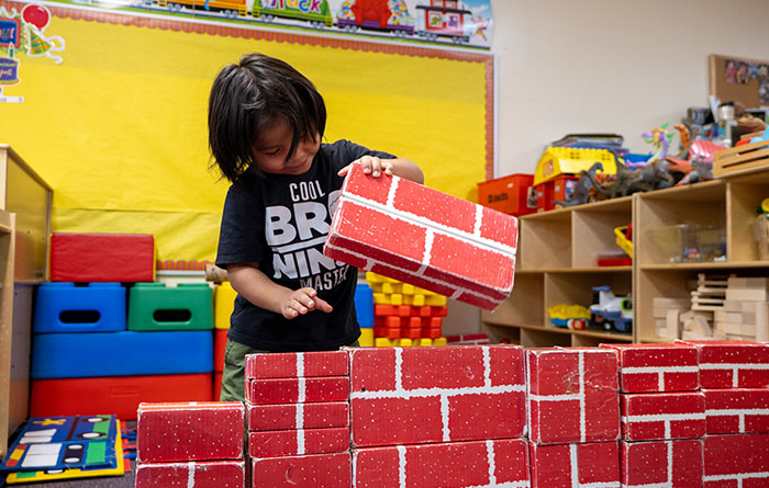 A young boy stacking large red blocks in a kindergarten classroom.