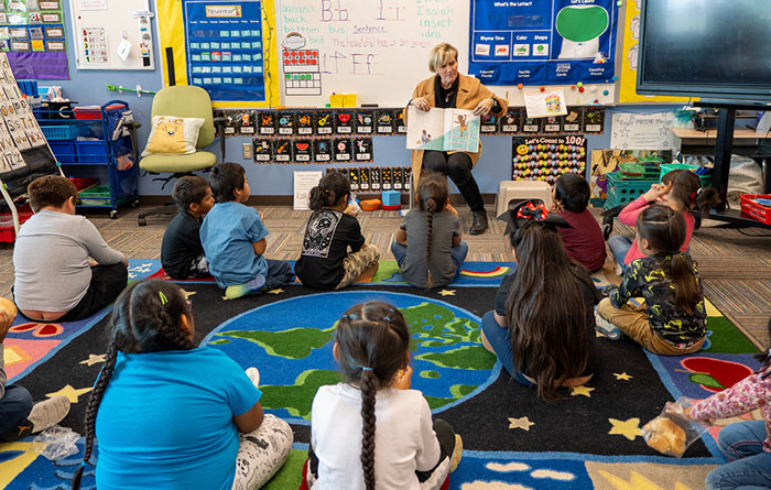 Teacher reading a book to a classroom of students sitting on the floor.