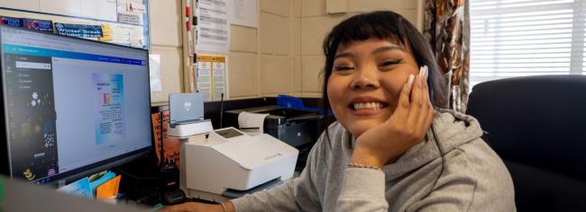 Happy student smiling at the camera in front of computer.